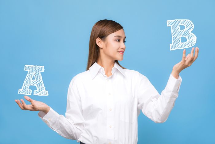 A woman stands in front of a blue background holding the letter A in one hand and B in the other, weighing them each as options.